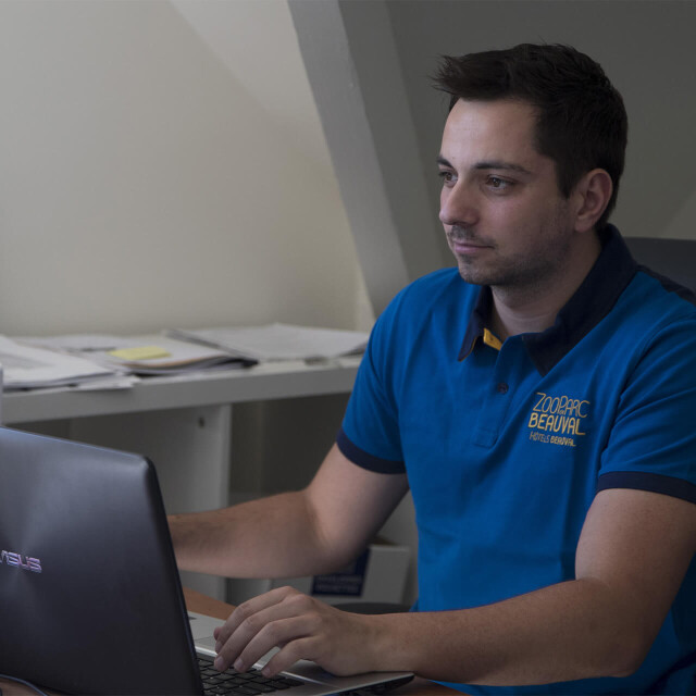 Métier du Zoo : Ressources Humaines - Emploi - ZooParc de Beauval - Employé consultant son ordinateur avec en fond le livret d’accueil pour les nouveaux salariés