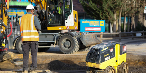 Métier du Zoo : Agent Technique - Domaine d'activité : Construction et Rénovation - Agent avec une machine à aplanir les sols et une pelleteuse en fond