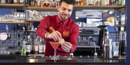 Métier des hôtels : Barman - Domaine d'activité : Salle - Barman préparant un cocktail avec une rondelle de citron en guise de décoration